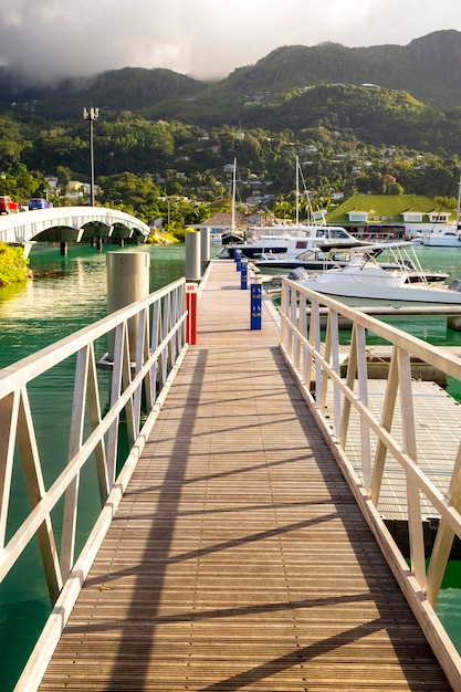 Muelle de madera y yates de lujo y barcos en un día soleado de verano en el puerto deportivo de Eden Island, Mahe, Seychelles, composición vertical