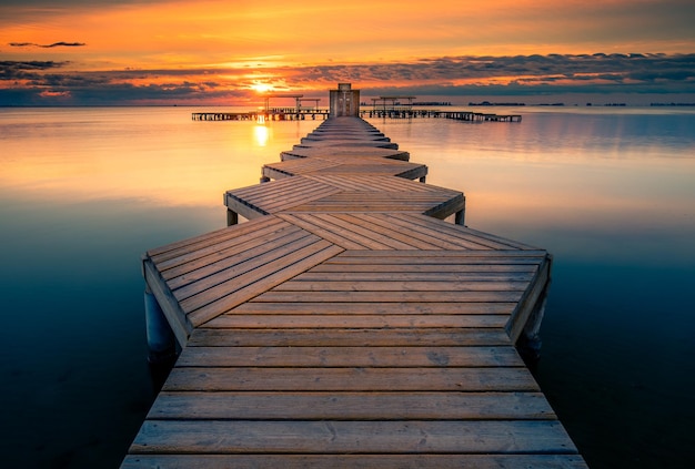 El muelle en el mar tranquilo contra la puesta de sol