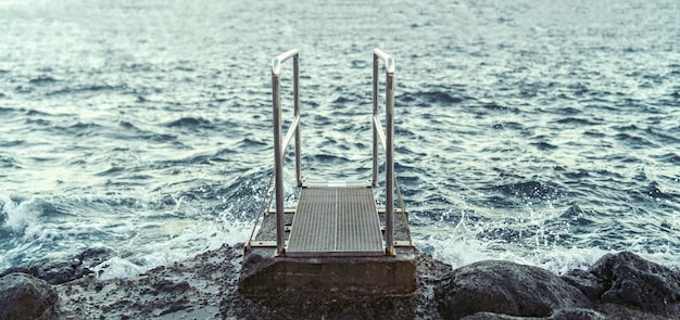 Muelle hacia el océano en la playa con piedras.