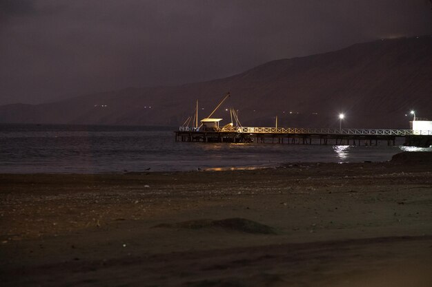 Un muelle en la playa por la noche con una montaña al fondo.