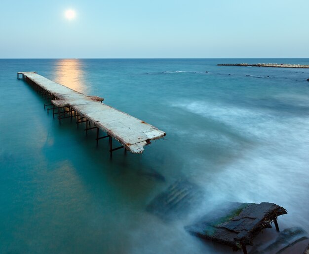 Muelle en ruinas, camino de la luna y costa de verano por la noche (Bulgaria).