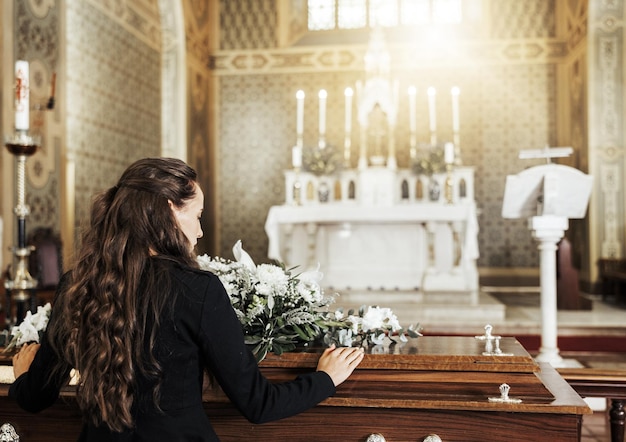 Muerte del ataúd funerario y mujer en la iglesia después de la pérdida de un amigo de la familia o un ser querido por cáncer Luto RIp y vista posterior de una mujer con flores en un ataúd de madera en la catedral para la ceremonia de entierro