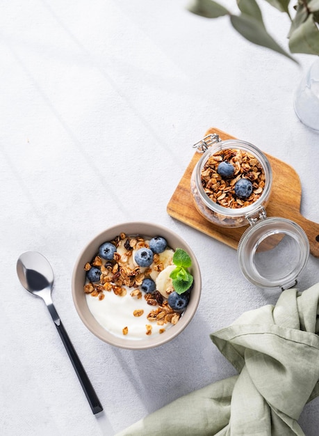 Muesli com iogurte vegetariano, banana e mirtilos em uma tigela em um fundo claro, granola caseira saudável e dietética para o café da manhã