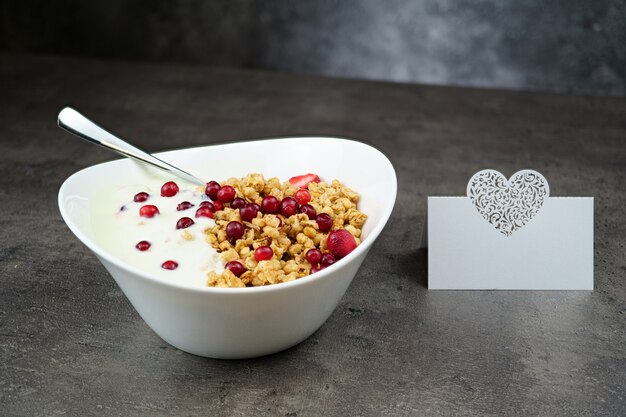 Muesli com srawberry e cranberry com iogurte em tigela branca sobre cinza