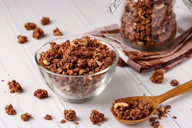 Muesli crujiente de granola con miel natural, chocolate y nueces en un recipiente de vidrio sobre un fondo blanco, comida sana, primer plano, orientación horizontal