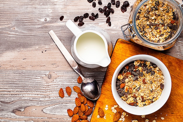 Muesli en el cuenco, jarra y jarra con leche en la mesa de madera.