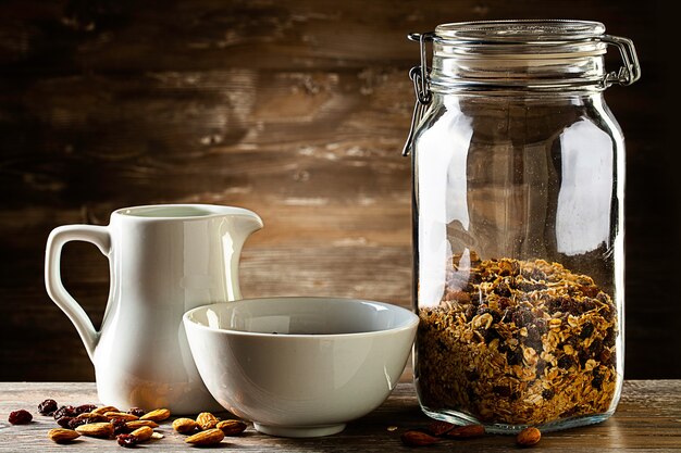 Muesli en el cuenco, jarra y jarra con leche en la mesa de madera.