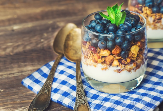 muesli de granola caseira com mirtilo e iogurte em copos em fundo de madeira rústico