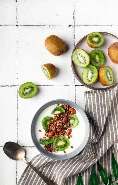 Foto muesli de granola caseiro com kiwi e iogurte em fundo de azulejos brancos taça de pequeno-almoço saudável