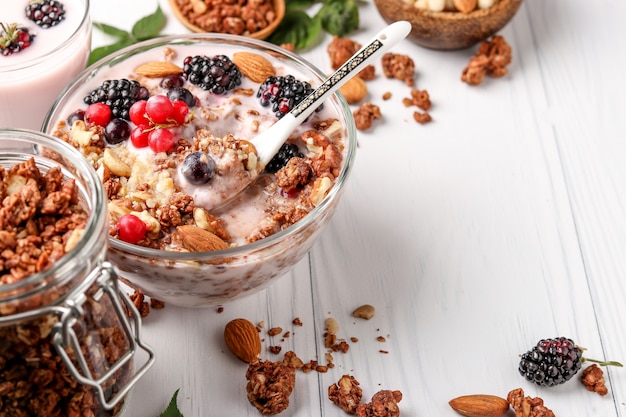 Muesli de mel crocante de granola com iogurte natural, frutas frescas, chocolate e nozes em uma tigela de vidro uma superfície leve