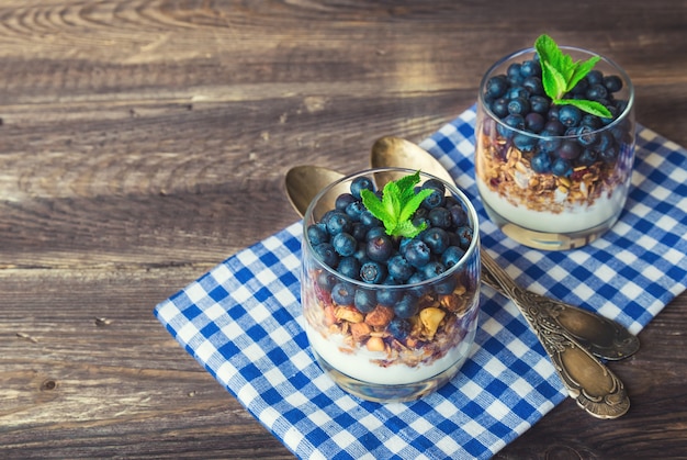 Muesli de granola casera con arándanos y yogur en vasos sobre fondo de madera rústica