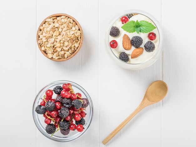 Müsli mit frischen Beeren und ein Glas Joghurt auf einem weißen Tisch