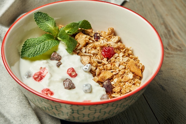 Müsli mit griechischem Joghurt und Beeren in einer Schüssel mit Leinentuch auf einer Holzoberfläche. Schließen Sie mit Platz für Text. Klassisches Frühstück