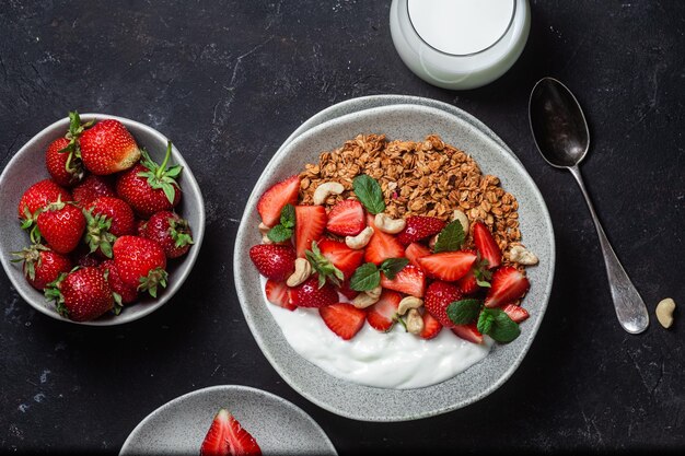 Müsli mit Joghurt und Erdbeeren auf einem Teller auf dunklem Hintergrund