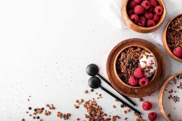 Müsli mit Schokolade, Nüssen und frischen Himbeeren in Holzschalen, Draufsicht