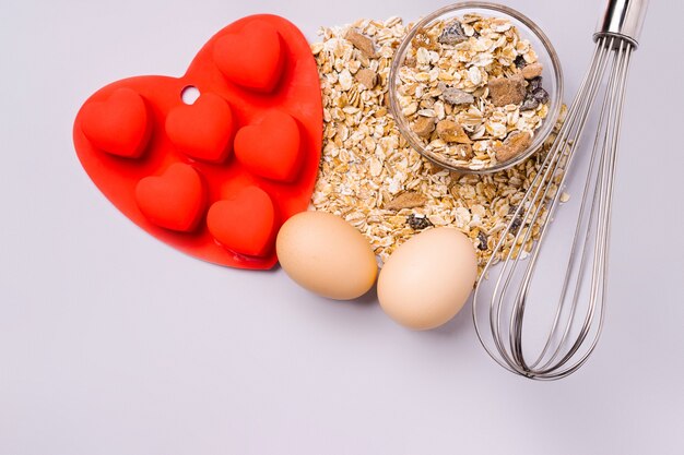 Müsli, Schneebesen und Auflaufform sorgen für eine köstliche Überraschung zum Valentinstag auf dem ultimativen grauen Hintergrund.