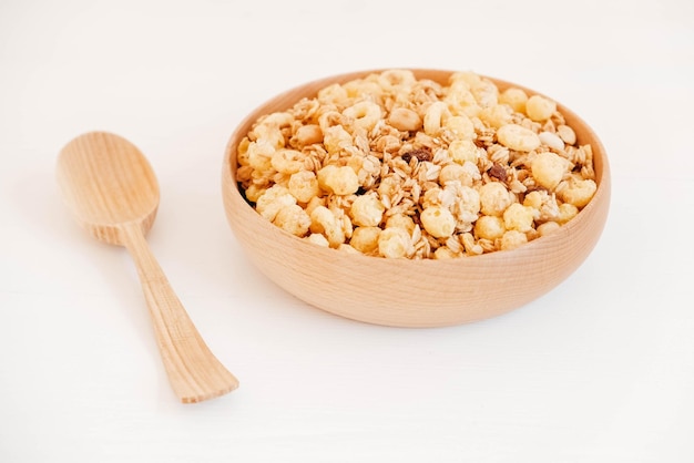 Muesli seco con copos de maíz, nueces y pasas en un tazón de madera sobre un fondo blanco