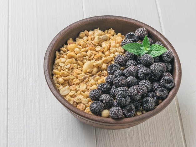 Müsli und schwarze Himbeeren in einer Tonschale auf einem weißen Tisch