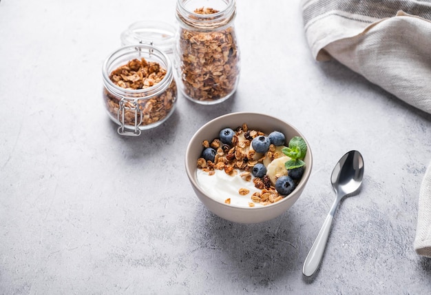 Muesli con yogur vegetariano, plátano y arándanos en un bol sobre un fondo gris Granola casera saludable y dietética para el desayuno