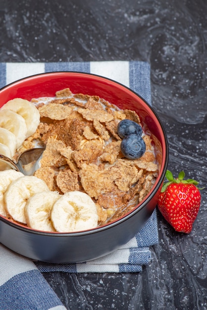 Müslifrühstück gesundes Essen und Diätmüsli mit Milch und Obst in einem Teller auf einer schwarzen Marmorplatte mit ...