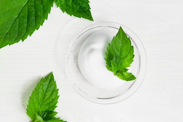Una muestra de crema corporal hidratante y tonificante sobre un fondo blanco con hojas verdes de menta fresca
