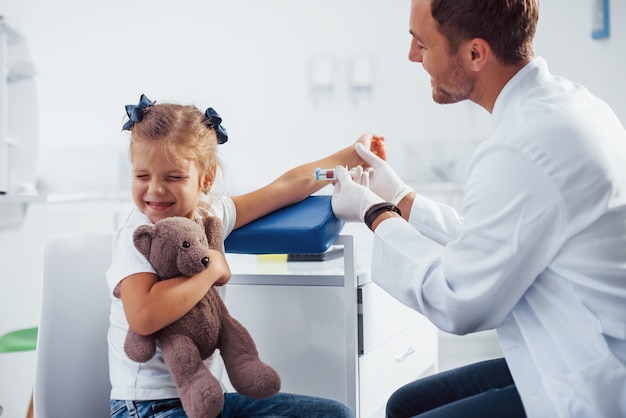 Muestra de sangre. La niña con su osito de peluche está en la clínica con el médico.