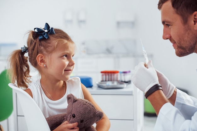 Muestra de sangre. La niña con su osito de peluche está en la clínica con el médico.