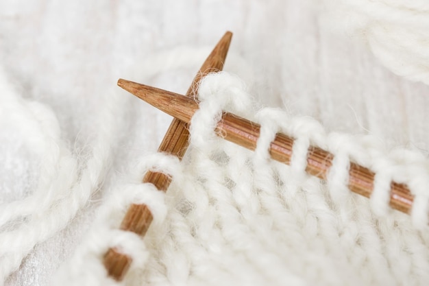 Muestra de tejido de hilo de lana de color blanco en agujas de tejer de madera sobre un fondo de madera
