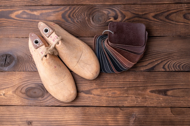 Muestras de cuero para zapatos y hormas de zapatos de madera en mesa de madera oscura.