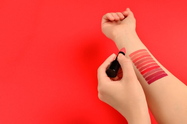 Muestras de lápiz labial en mano de mujer aislado sobre fondo rojo.