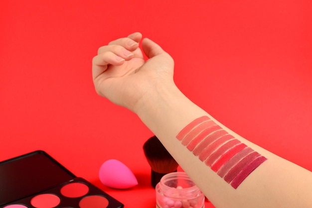 Muestras de lápiz labial en la mano de la mujer Productos de maquillaje profesional con productos cosméticos de belleza base lápiz labial sombras de ojos pestañas cepillos y herramientas