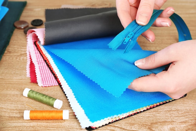 Muestras de telas coloridas y cremallera en manos femeninas sobre fondo de mesa de madera