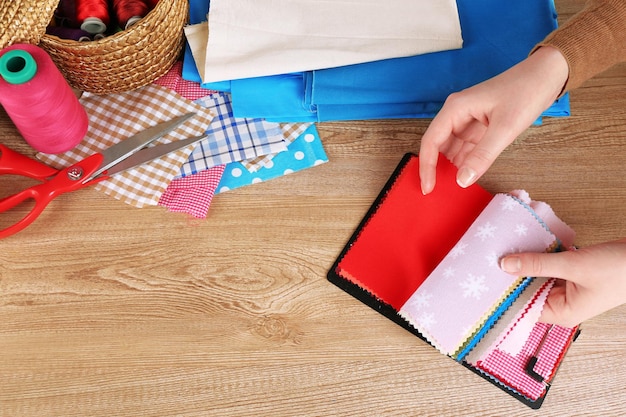 Muestras de telas coloridas en manos femeninas y detalles para coser en fondo de mesa de madera