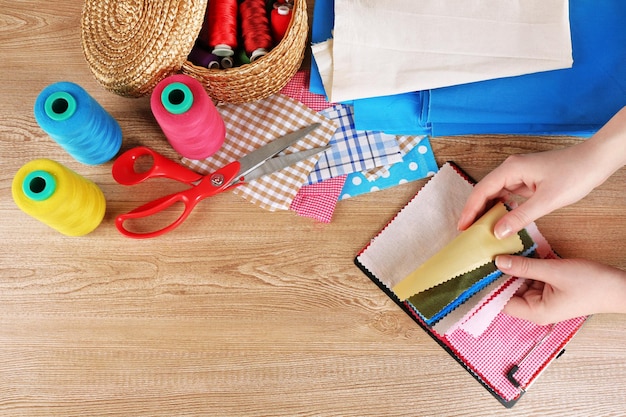 Muestras de telas coloridas en manos femeninas y detalles para coser sobre fondo de mesa de madera