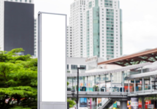 Muestre una cartelera vertical con pantalla LED blanca en el poste de la torre con un trazado de recorte de la vista del paisaje urbano