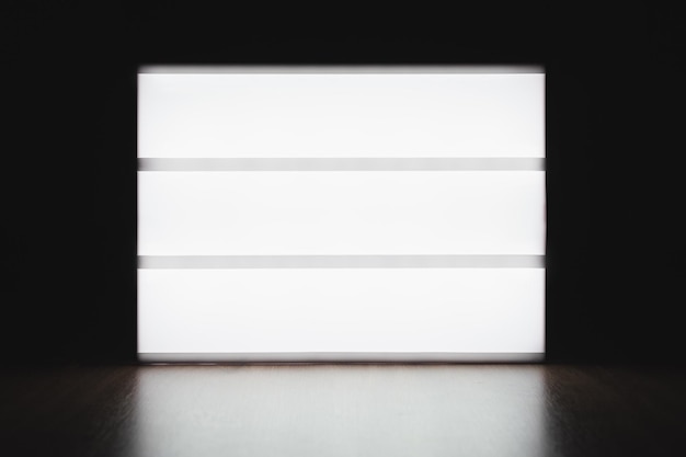 Muestre la pantalla luminosa de la caja de luz sin letras sobre la mesa en la oscuridad