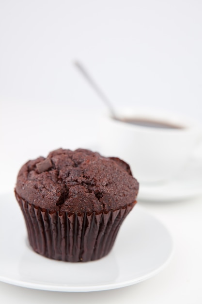 Muffin de chocolate y una taza de café con una cuchara en platos blancos