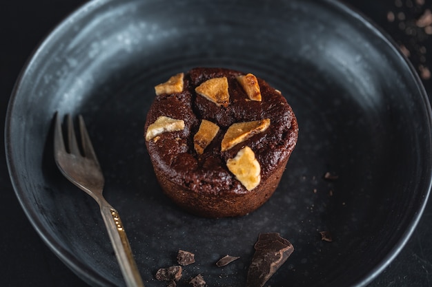 Muffin de chocolate con trozos de plátano en un plato oscuro con un tenedor. De cerca