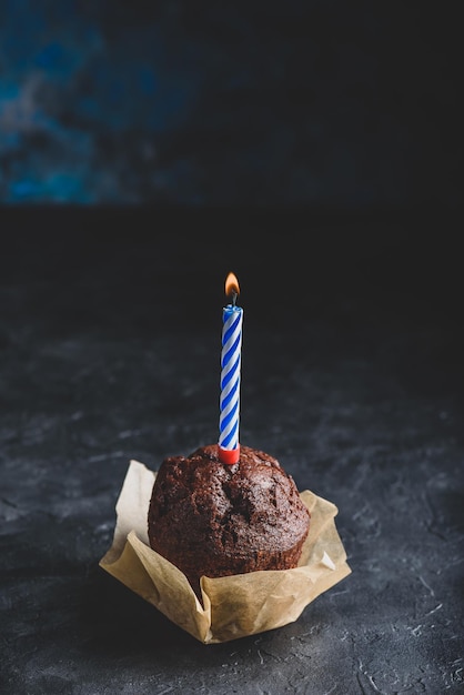 Muffin de chocolate con vela de cumpleaños sobre fondo de hormigón oscuro