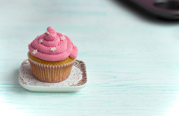 muffin con crema de color lila decorado con perlas comestibles se encuentra sobre un fondo de madera.