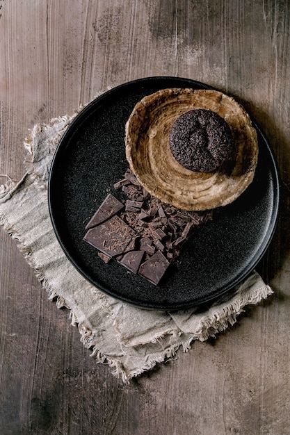 Muffin de cupcake de chocolate casero con chocolate negro picado en placa de cerámica negra sobre fondo de textura de hormigón. Endecha plana, espacio de copia