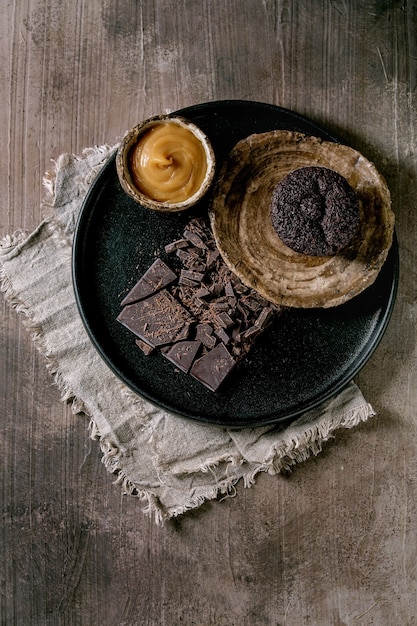 Muffin de cupcake de chocolate casero con salsa de caramelo salado y chocolate negro picado en placa de cerámica negra sobre tabla de textura de hormigón. Lay Flat, espacio de copia