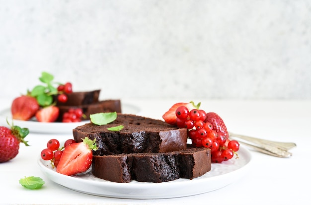 Muffin de chocolate com morangos e groselhas em um fundo claro de concreto. Pedaços de bolo. Torta de brownie.