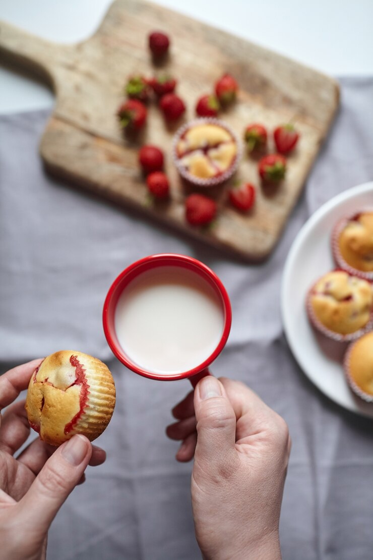Muffin de fresa con taza de leche en las manos sobre la mesa de la cocina