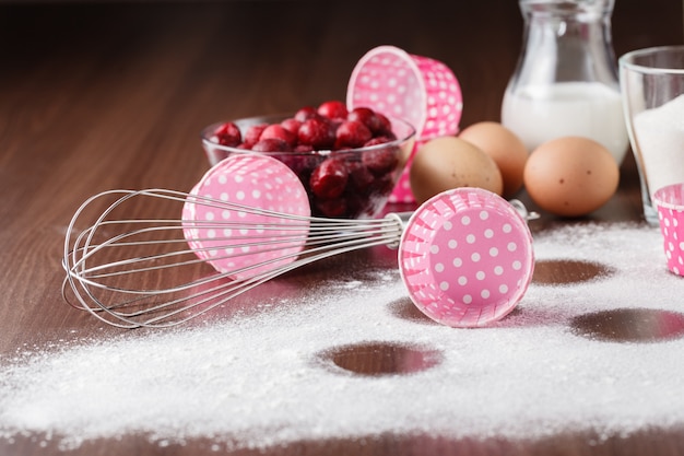 Muffin ingredientes: a cereja congelada em um prato, ovos, farinha em uma mesa de madeira escura