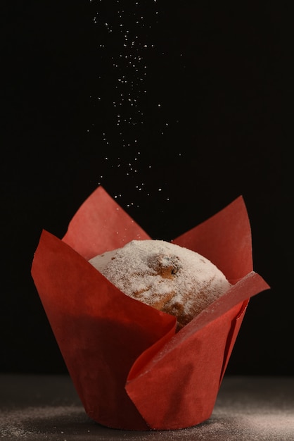 Un muffin en papel de hornear rojo se encuentra en una mesa.