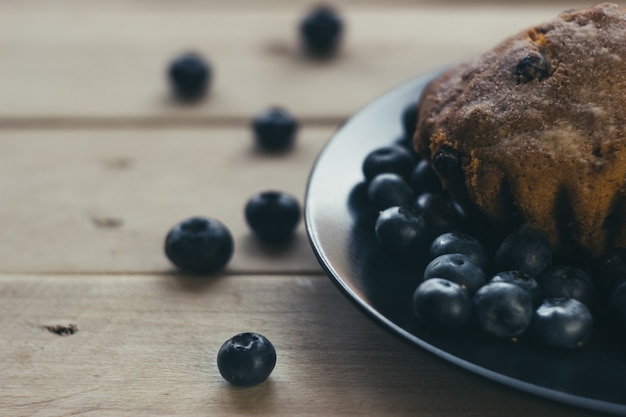 Muffins de arándanos con azúcar glass y frutos rojos frescos. Los arándanos frescos están esparcidos sobre la mesa de madera