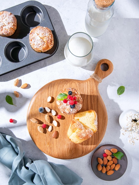 Muffins caseiros acabados de cozer com nozes e bagas numa tábua de madeira sobre uma mesa de luz com leite e amêndoas