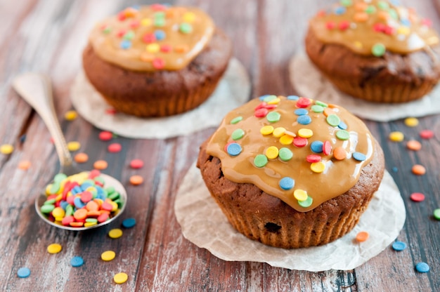 Muffins de chocolate Con caramelo y toques multicolores Geometría Un fondo de madera está borroso