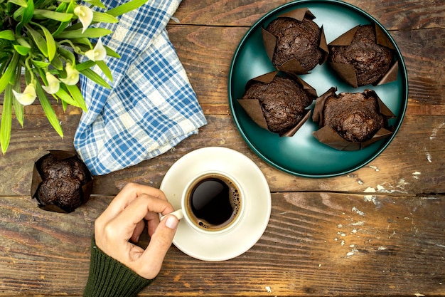 muffins de chocolate caseros o madeleine en plato verde y mujer bebiendo un café lirios flores o